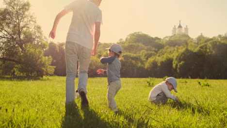 A-young-father-in-a-white-t-shirt-with-two-sons-playing-football-on-the-grass-at-sunset-in-the-sun-in-slow-motion